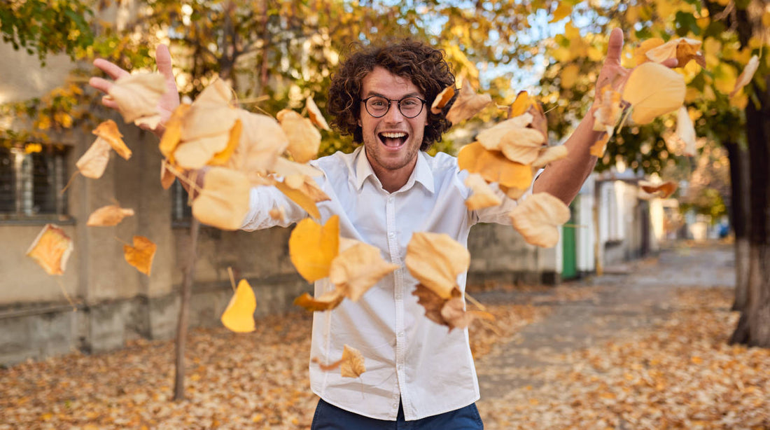 Man with long hair during autumn throwing leaves