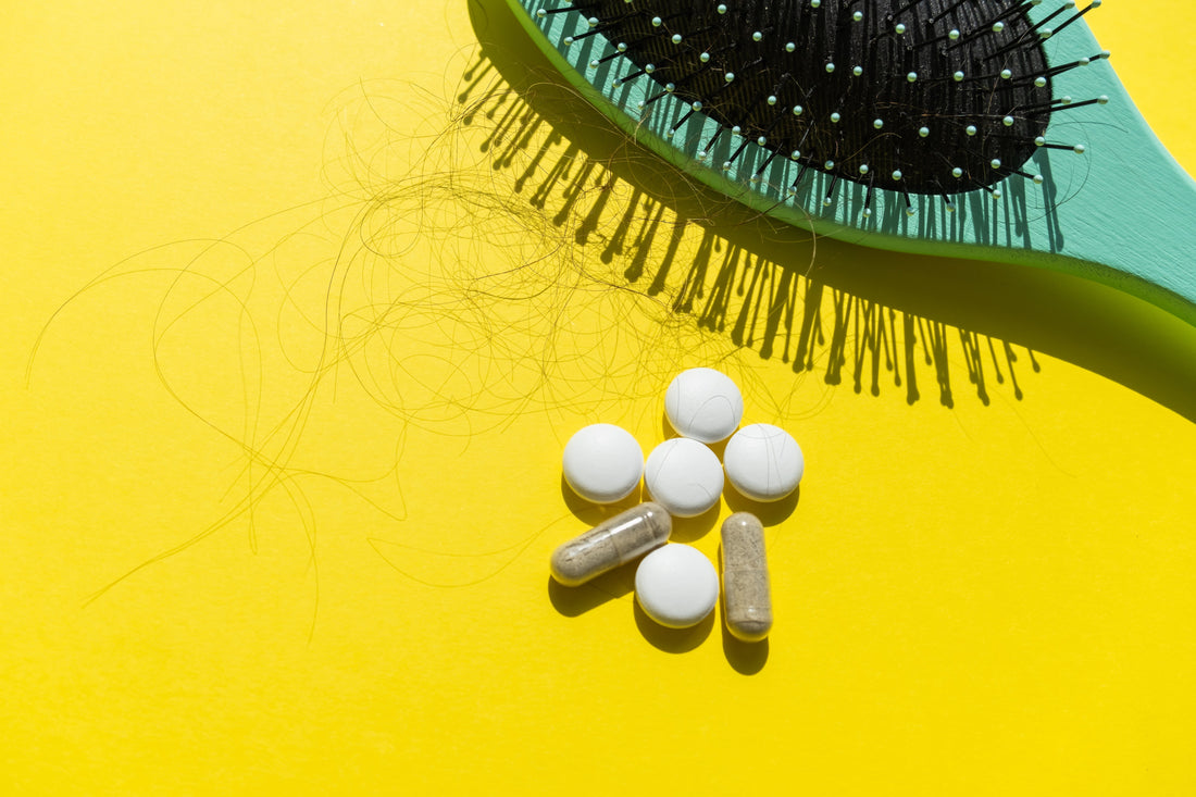 A blue hair brush, loose hairs, and a variety of pills lay on a yellow background.