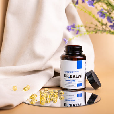Eine Flasche Dr. Balwi Shop Vitamin D 1000 IE mit offenem Deckel steht auf einer spiegelnden Fläche, weiche Gelkapseln liegen verstreut daneben - ideal, um das Immunsystem zu stärken. Im Hintergrund sind lila Blumen und ein weißes Tuch zu sehen.