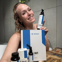 Eine lächelnde Frau mit nassem Haar hält eine Flasche Dr. Balwi-Haarpflegeprodukt und posiert mit einem Set von Elithair-Markenprodukten, während sie in einem Badezimmer sitzt.