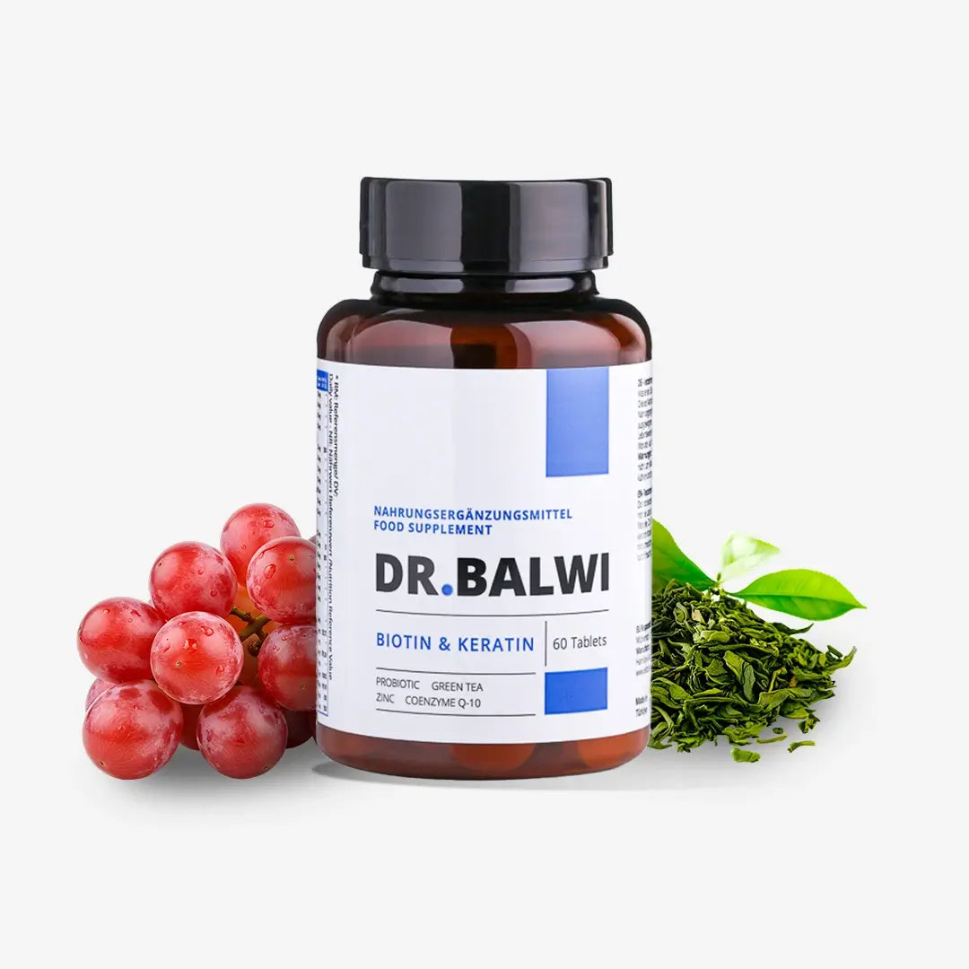 Eine Flasche Biotin & Keratin Tabletten aus dem Dr. Balwi Shop ruht auf einer weißen Fläche, umgeben von roten Trauben und grünen Teeblättern - ideal für alle, die Haarwachstum mit Unterstützung von Biotin Tabletten suchen.